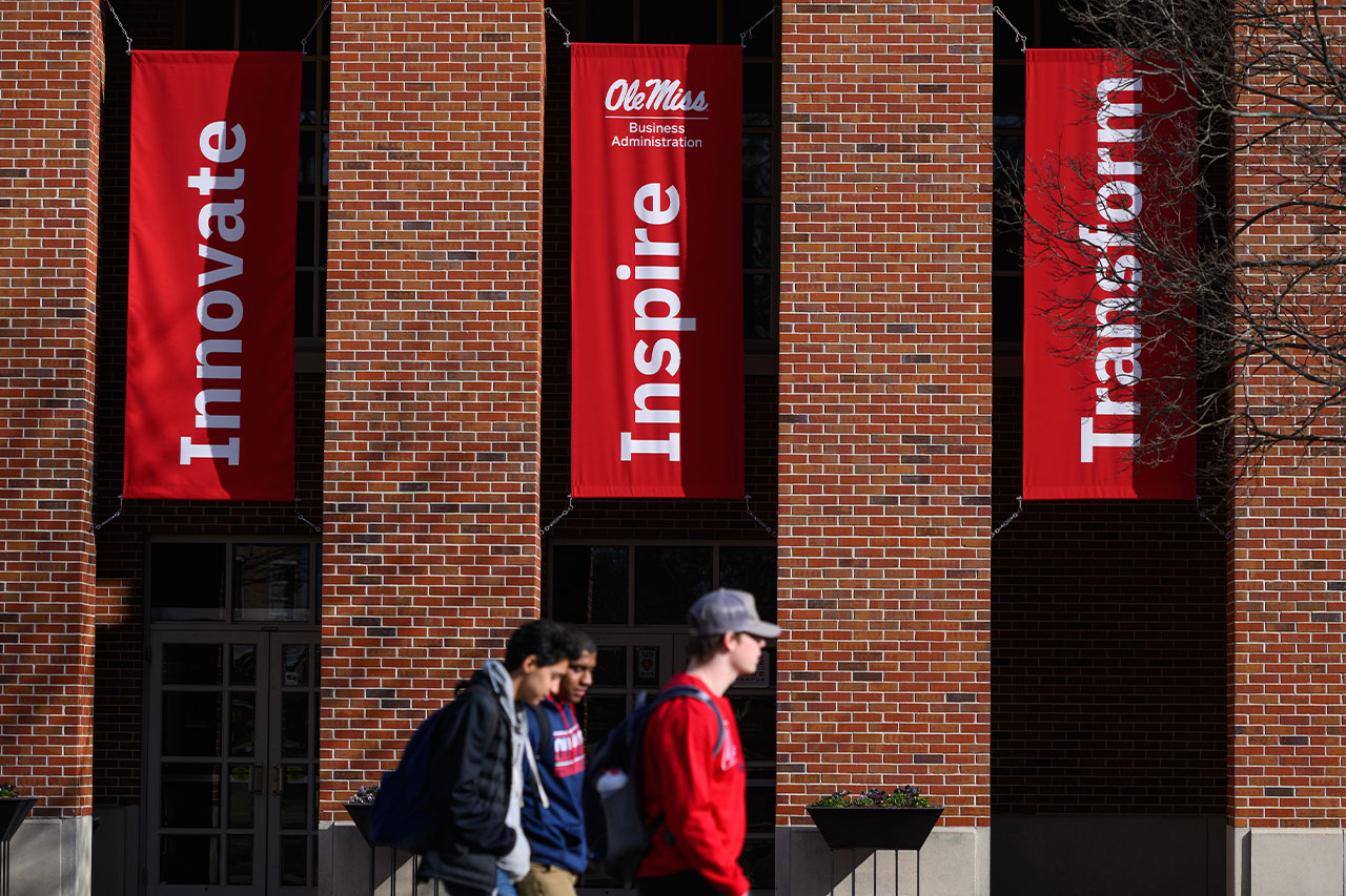 Three students walking across Holman Hall with the banners int he background.