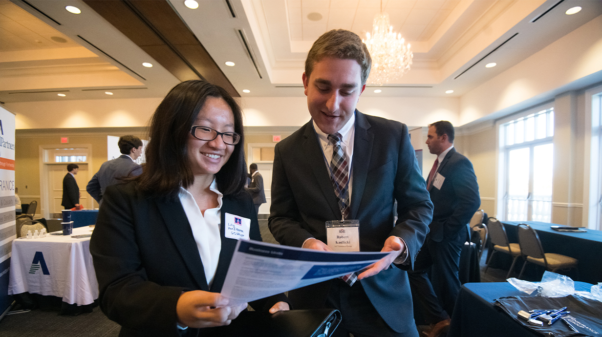 A student and an employer during a career fair discussing a leaflet.