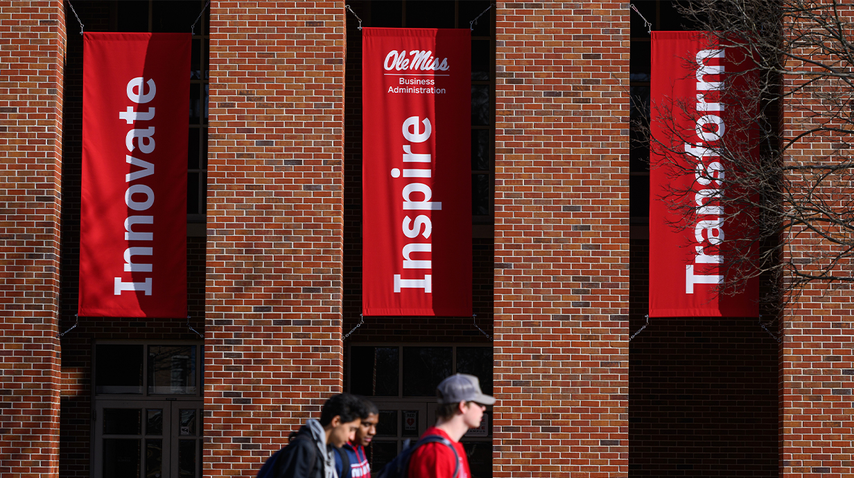 Innovate, Inspire, and Transform banners outside Holman with three students walking in the foreground.