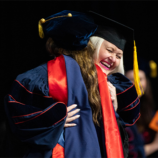 Two individuals hugging during the doctoral hooding ceremony.