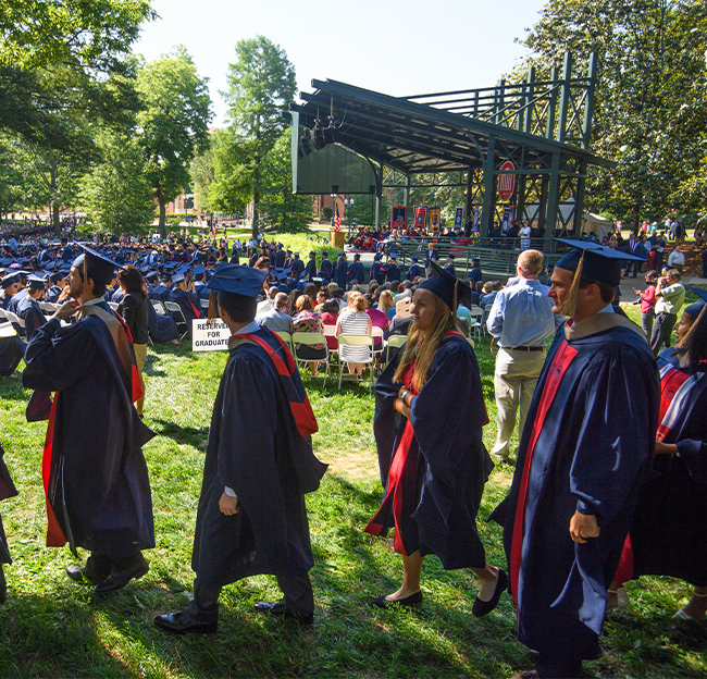 A line of graduate students walking through the Grove during a commencement.