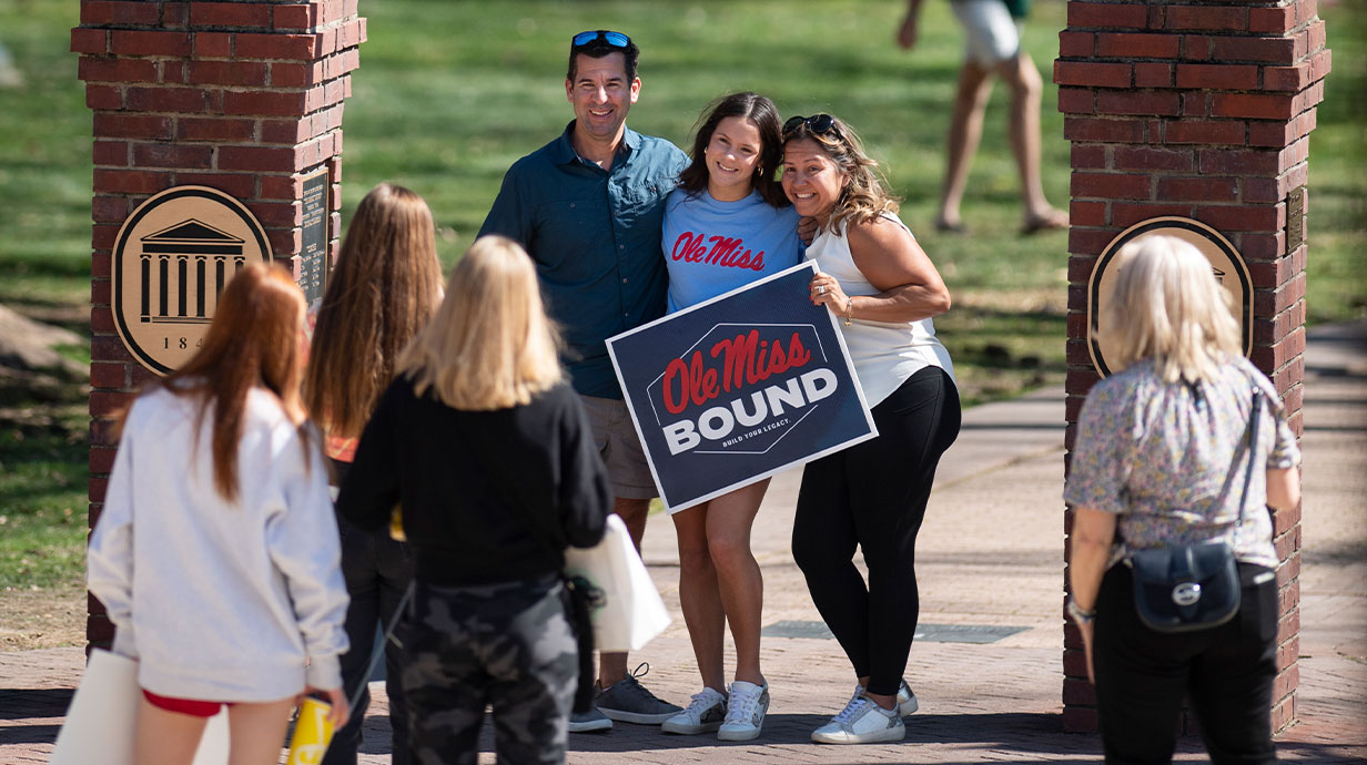 A family posing in front of the Walk of Champions with an Ole Miss Bound sign.