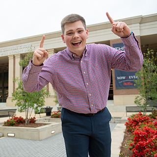 Student in front of the Student Union pointing up with both hands.