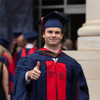 Graduate MBA student giving a thumbs up outside the Ford Center.