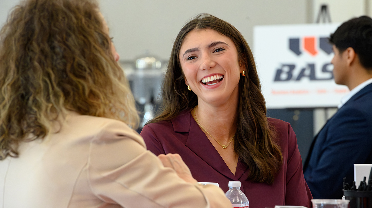 A young woman smiles and talks to another woman in a convention hall.