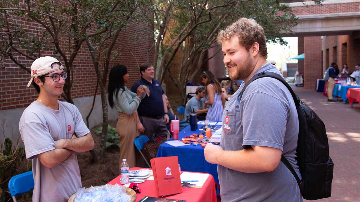 An MBA graduate candidate (left) speaking with a student (right) during an Open for Business event in the Holman courtyard.