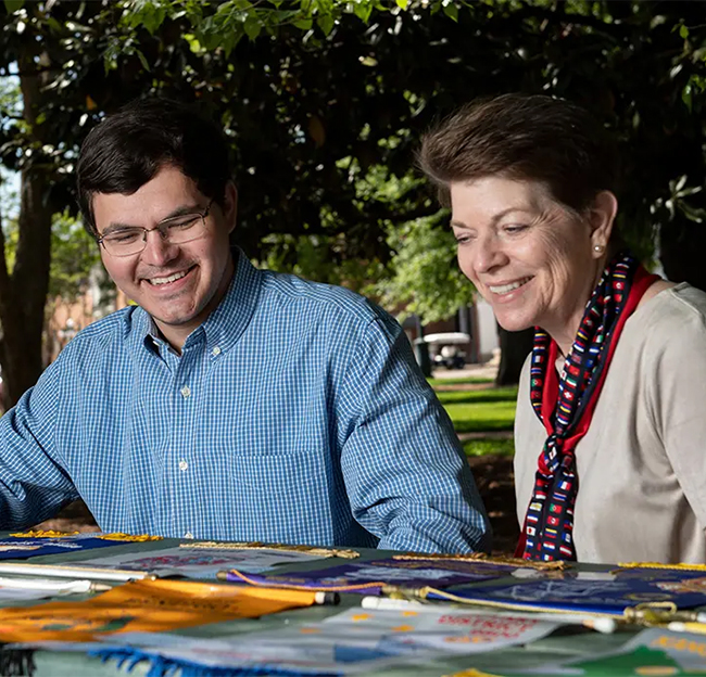 Man and woman sit at a picnic table looking at colorful banners.