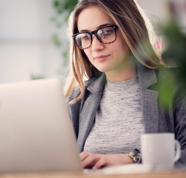 A female student with glasses taking notes or interviewing in front of a laptop.