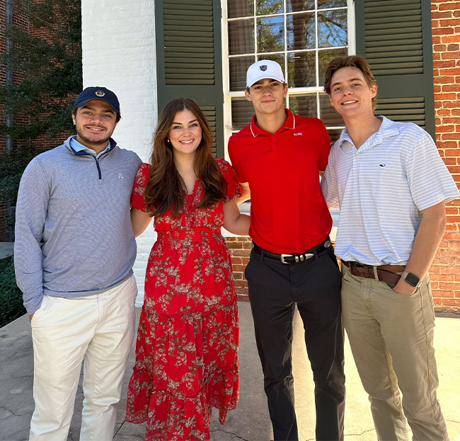 A group of students, three males and one female taking a group photo.